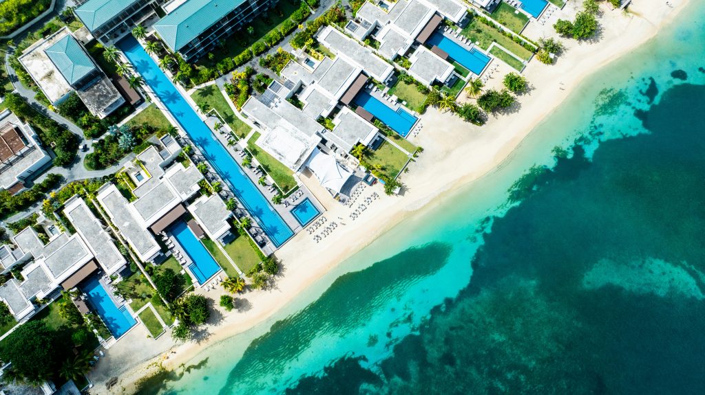 Grand hôtel resort avec piscine et palmiers dans les Antilles, illustrant le luxe et le service inclus de l'option location ou hôtel aux Antilles.